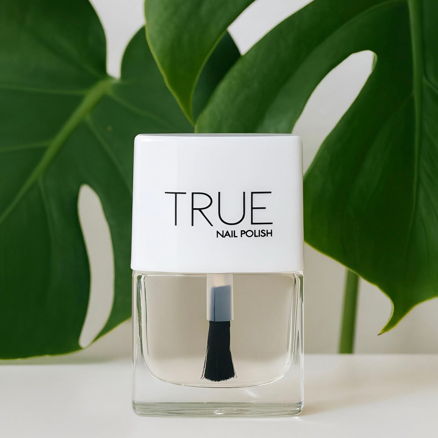 Clear nail polish bottle with white cap labeled 'TRUE' against a green leafy background
