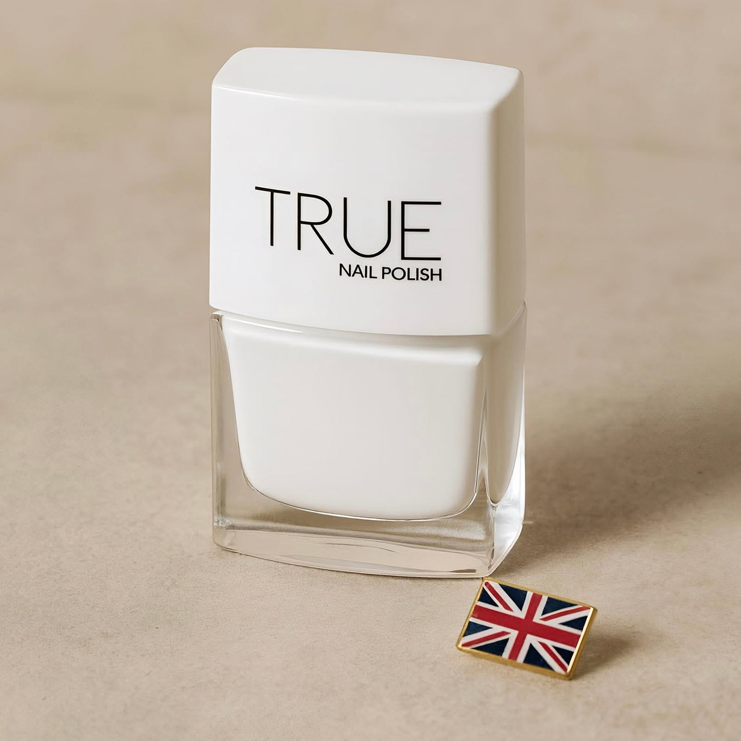 White nail polish bottle labeled 'TRUE' with a Union Jack pin on a beige background