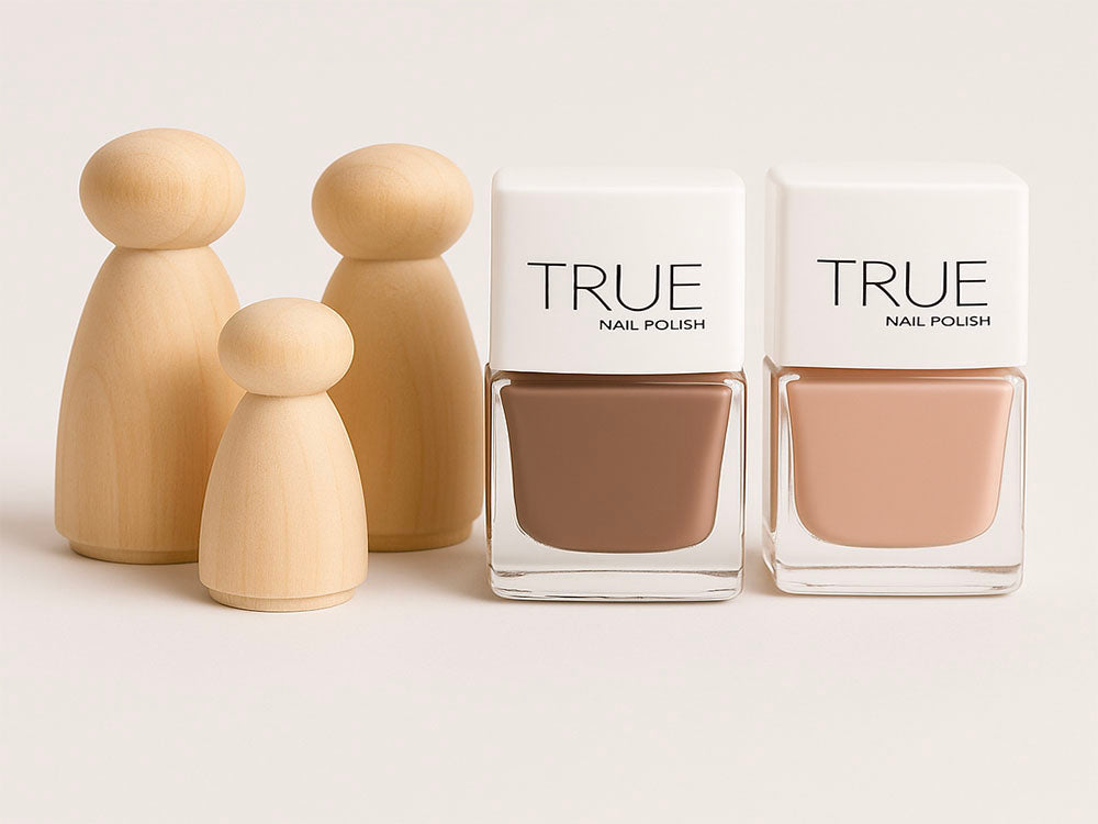 Two bottles of True nail polish with beige nail polish color on a light background, accompanied by wooden dolls.