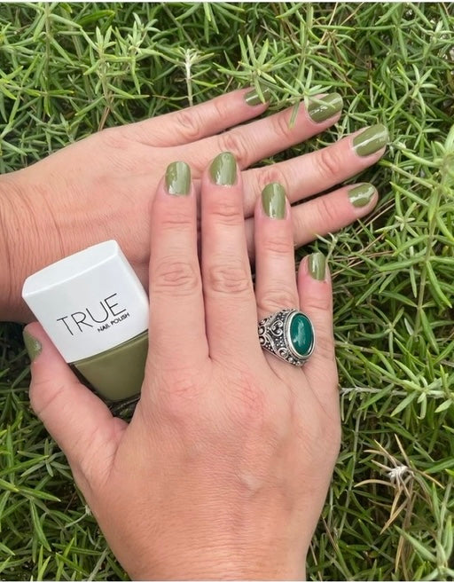 manicure wearing true nail polish outlaw, a khaki green vegan, plant-based nail polish. Hands wearing cocktail silver ring with green stone, and holding a bottle of true nail polish.