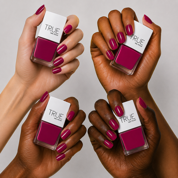 Four hands of different skin tones holding TRUE nail polish bottles with a deep magenta-pink polish called señorita , a gel like, long wearing nail polish. shown on the nails and in the bottle, against a light gray background.