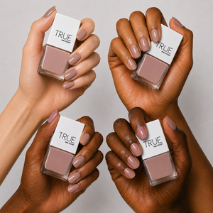 Four hands holding True Nail Polish bottles with sugar & spice, a dusty mauve-pink , mink, soft nude nail polish, shown against a light gray background.